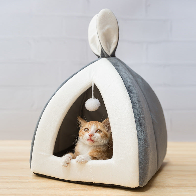 A small cat peeking out from a gray and white pet house with a hanging toy.