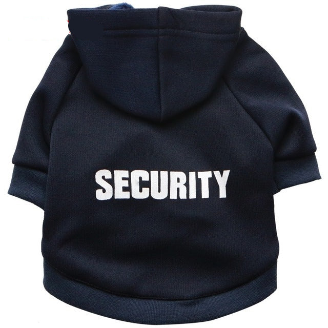 Two cats wearing black hoodies with the word 'SECURITY' written across the back in white letters. One cat is facing away, looking out a window, and the other is sitting facing forward.