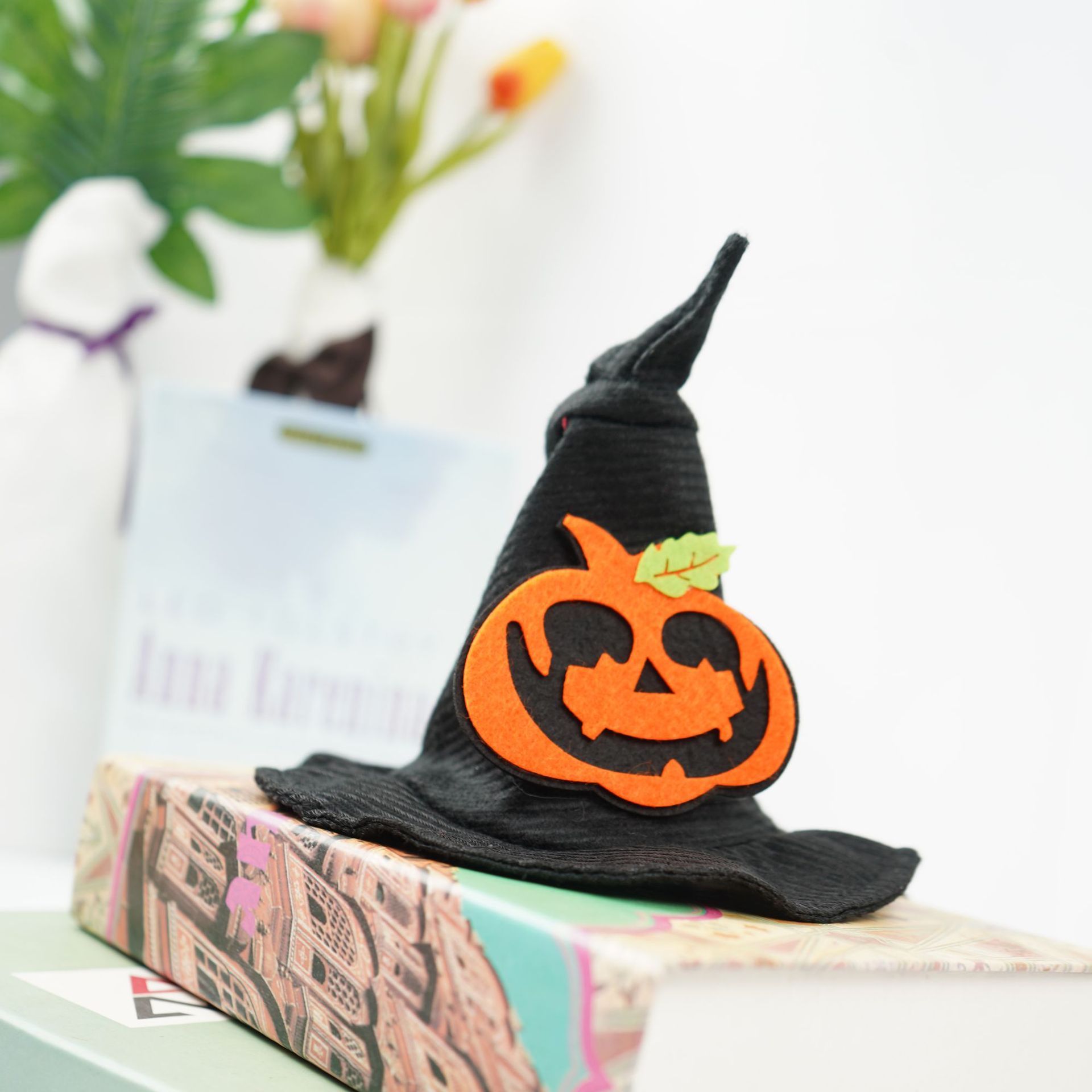 A black pet hat with a pumpkin design on it, placed on a surface with a blurred background.