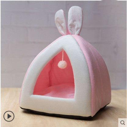 A small cat peeking out from a gray and white pet house with a hanging toy.