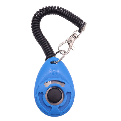 A selection of pet training clickers in various colors with a key ring, attached to a spring cord, and being used by a person training a dog.