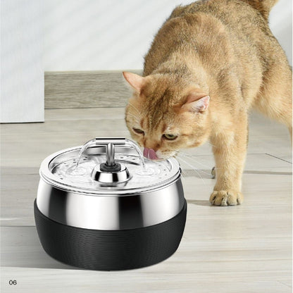 A cat using a silver stainless steel water dispenser with a black base.
