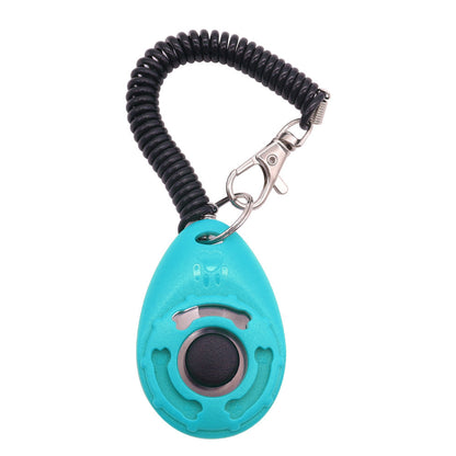 A selection of pet training clickers in various colors with a key ring, attached to a spring cord, and being used by a person training a dog.